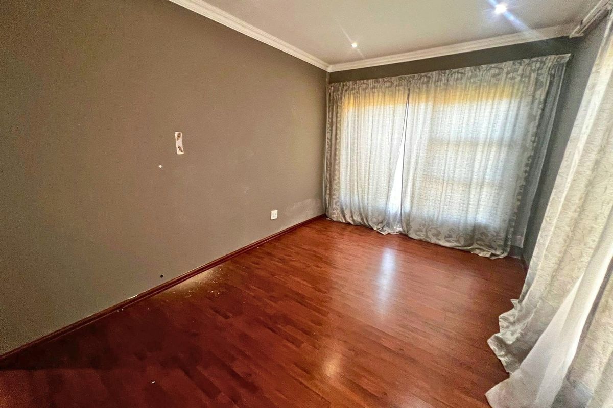 A vacant bedroom featuring dark wood-look laminate flooring, neutral wall paint, and large window with curtain tracks.