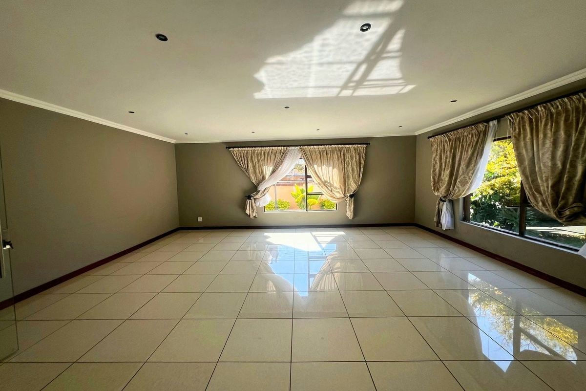 A spacious, empty living room featuring large format floor tiles, recessed downlighting, and expansive windows that provide ample natural light.