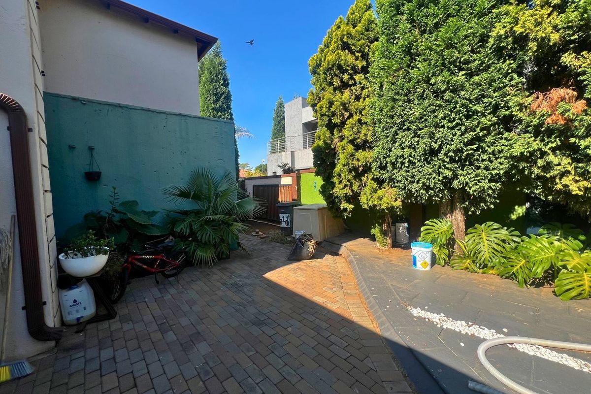 A paved rear courtyard area featuring a boundary wall, mature trees, and established garden beds.