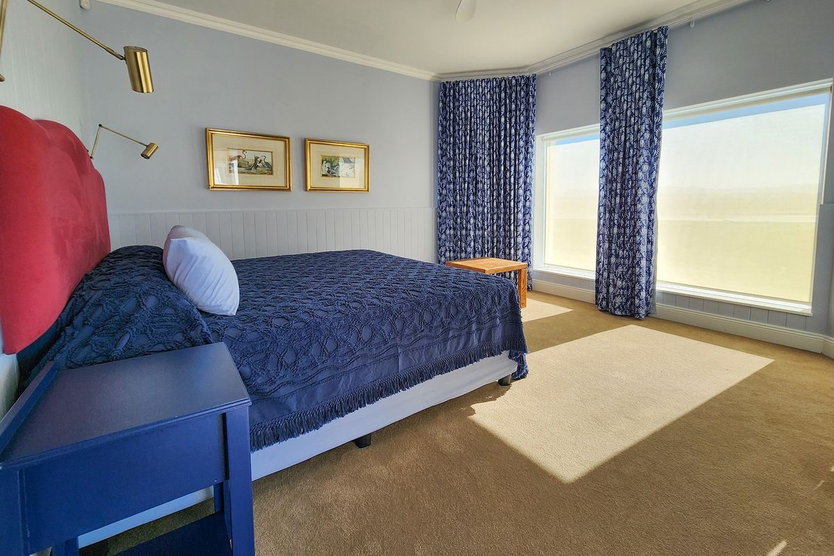 Spacious bedroom featuring large windows with natural light, neutral carpeting, and classic wall paneling details.