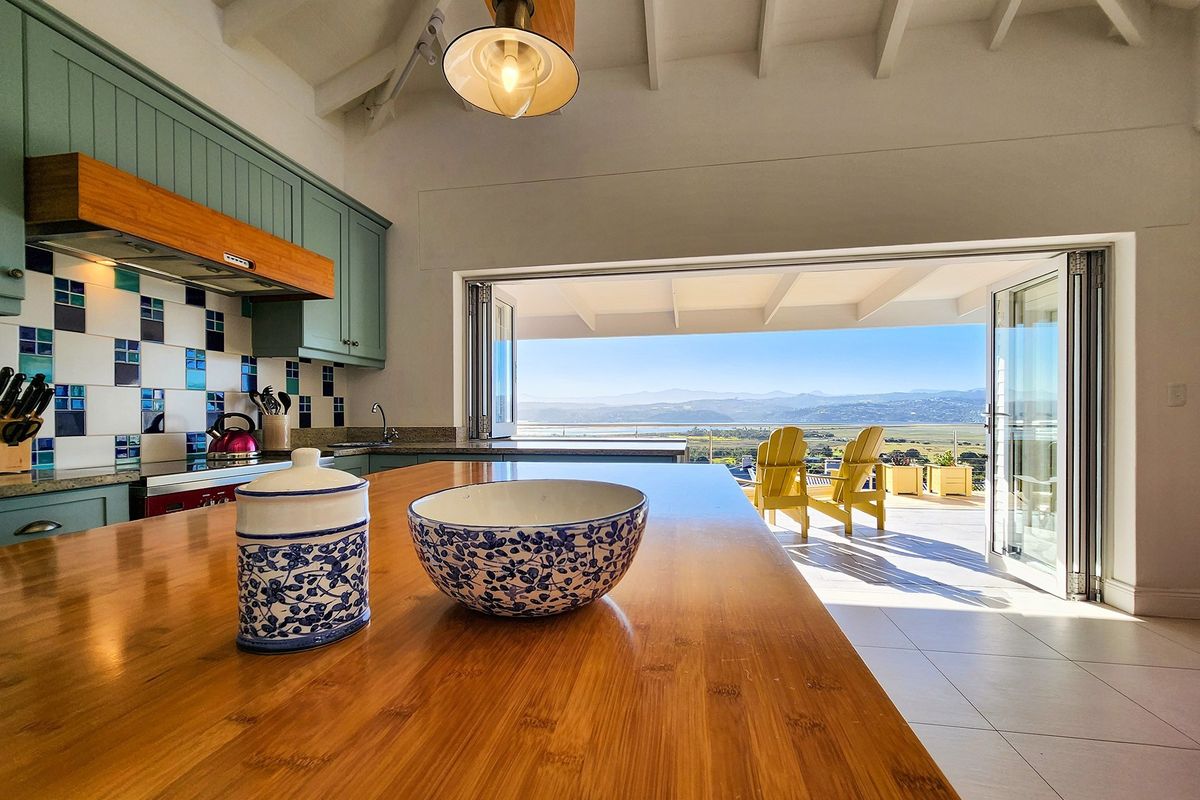 A bright kitchen featuring a wooden island, custom cabinetry, and a tiled backsplash, opening directly onto a patio with expansive mountain and landscape views.