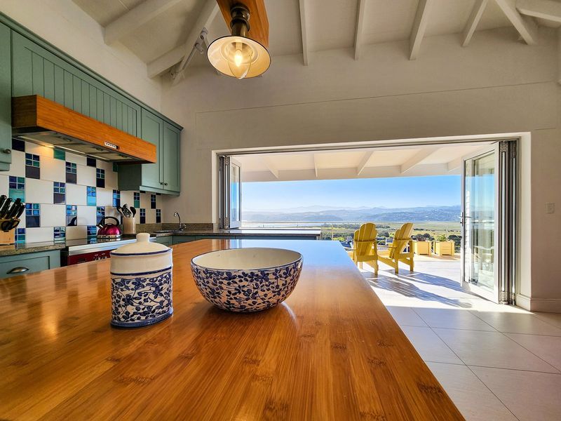 A bright kitchen featuring a wooden island, custom cabinetry, and a tiled backsplash, opening directly onto a patio with expansive mountain and landscape views.
