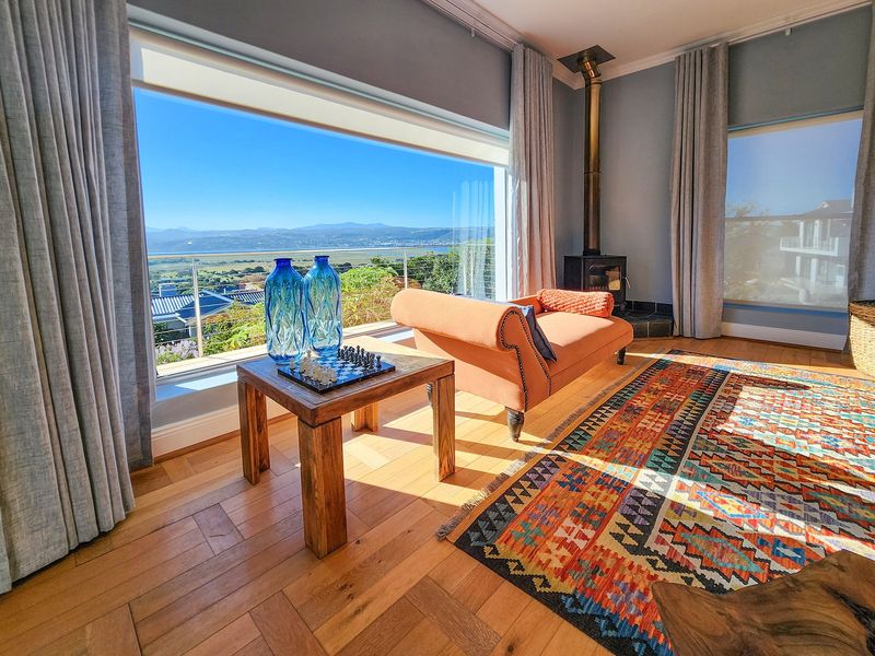 A bright living room featuring large picture windows with panoramic landscape views, hardwood flooring, and a built-in wood-burning fireplace.