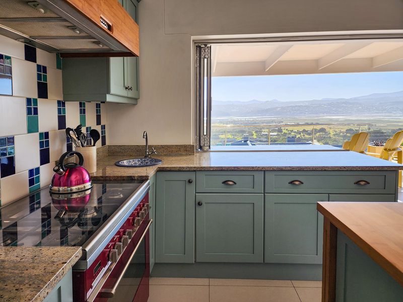 A well-appointed kitchen featuring light blue cabinetry, granite countertops, a built-in stove, and a large window opening to a scenic landscape view.