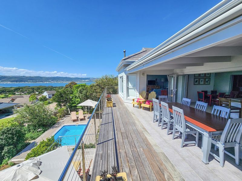Spacious covered patio with timber decking and tiled flooring, offering expansive elevated views over the garden, swimming pool, and surrounding landscape.