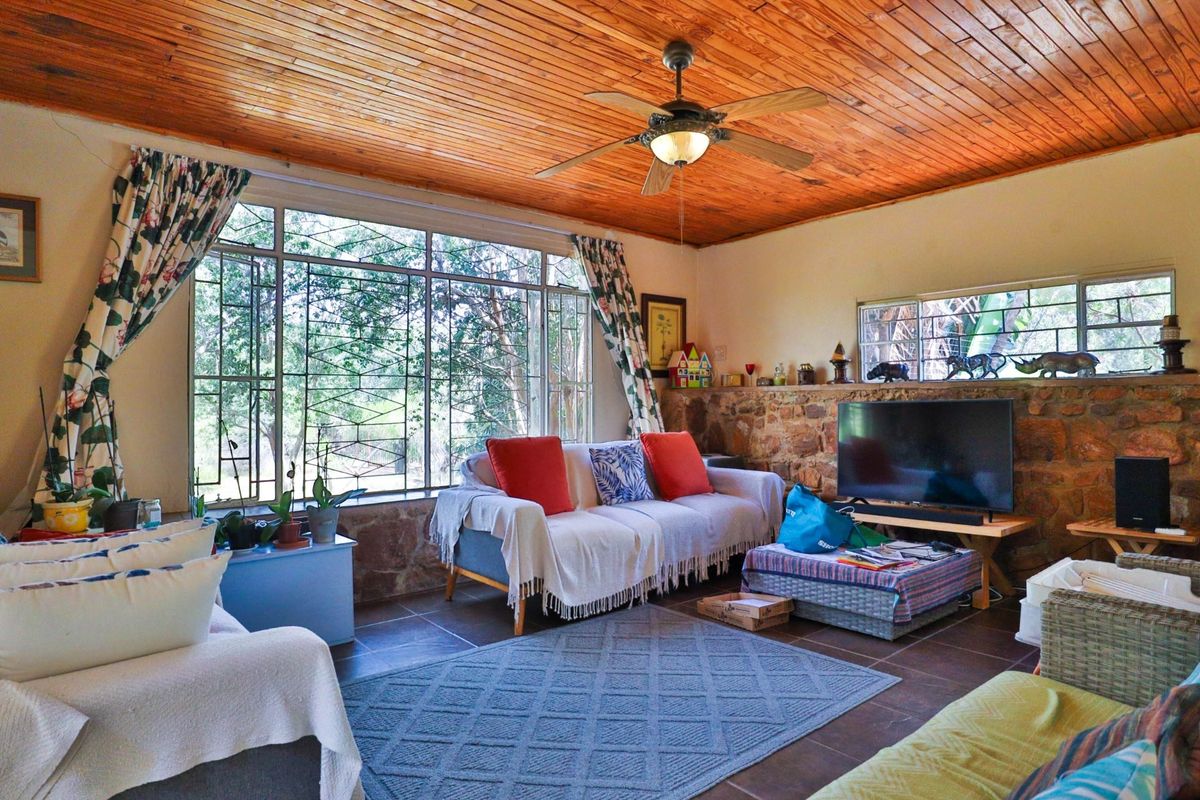 A cozy living room featuring a rustic stone feature wall, large windows with security bars, and a warm timber-clad ceiling with a central fan.
