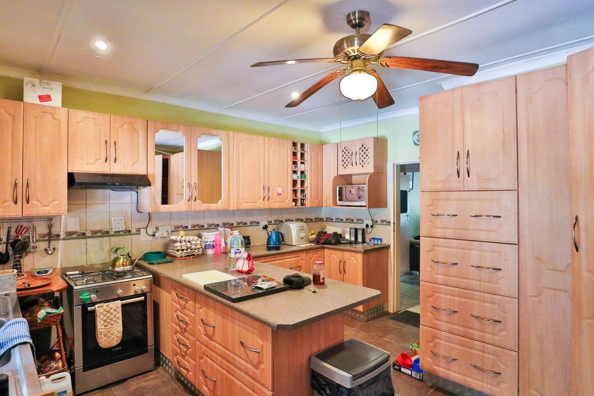 A functional kitchen featuring light wood cabinetry, a built-in oven with extractor fan, stone-look countertops, and a ceiling fan.
