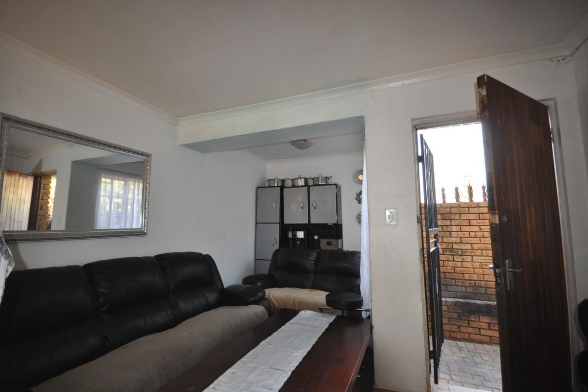 A living room area featuring a security gate entrance, timber door, and cove cornicing, requiring cosmetic updates to improve the overall finish.
