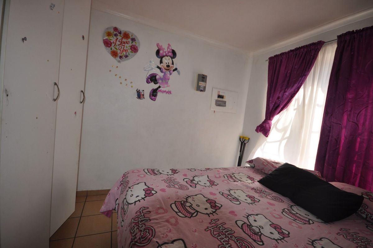 A functional bedroom featuring built-in cupboards and tiled flooring, offering a practical space with potential for cosmetic updates.