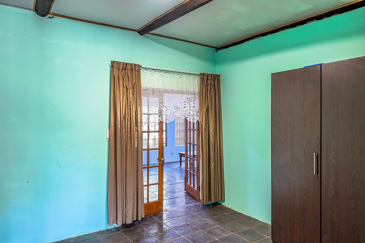 A bedroom featuring tiled flooring, exposed ceiling beams, and double wooden doors leading to an adjacent room.