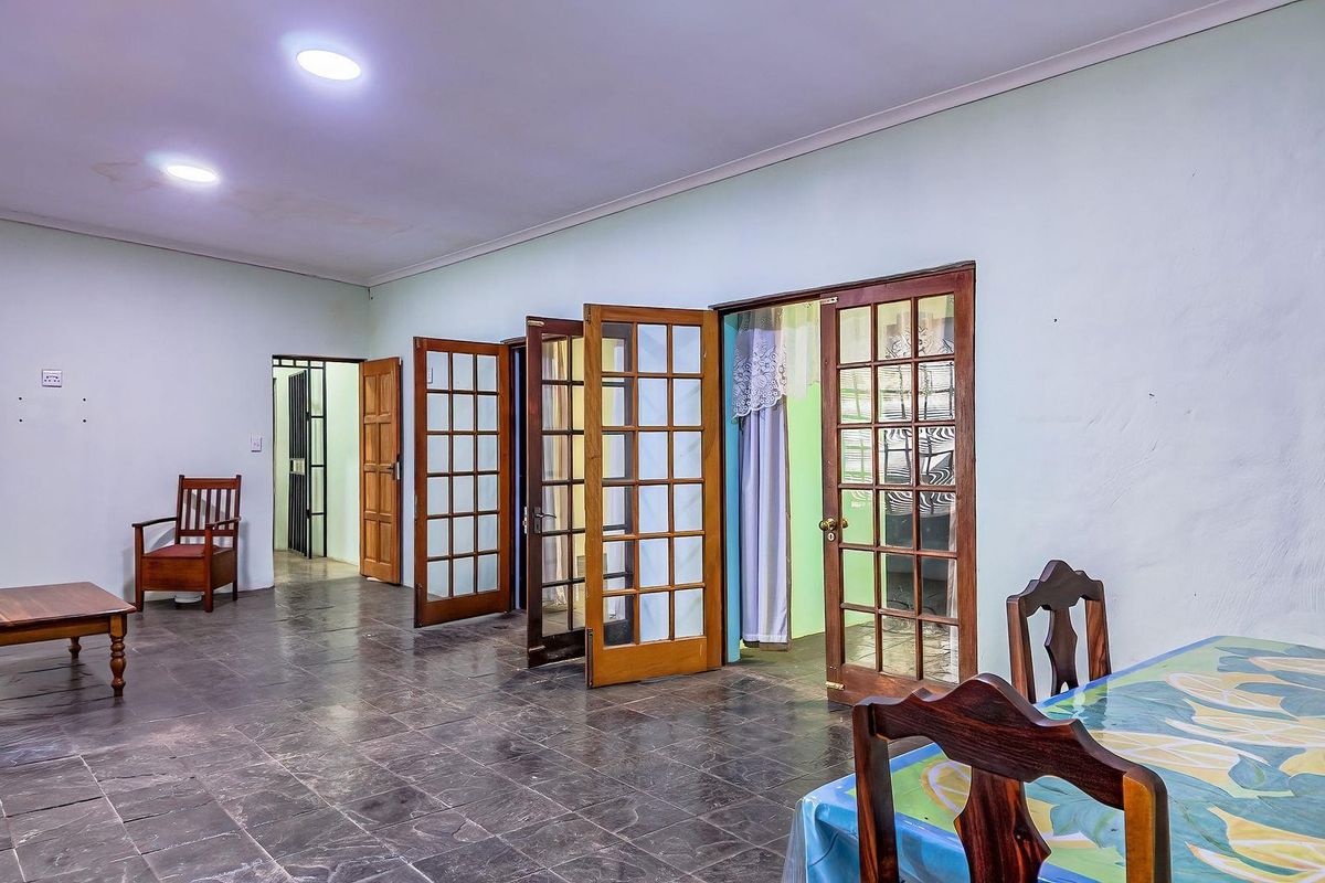 Spacious living area featuring dark tiled flooring, multiple wooden French doors providing access to adjacent rooms, and recessed ceiling lighting.