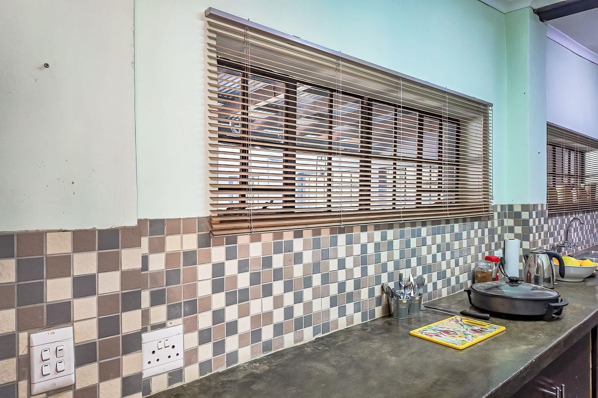 A functional kitchen area featuring a dark countertop, mosaic tile backsplash, and horizontal window blinds.