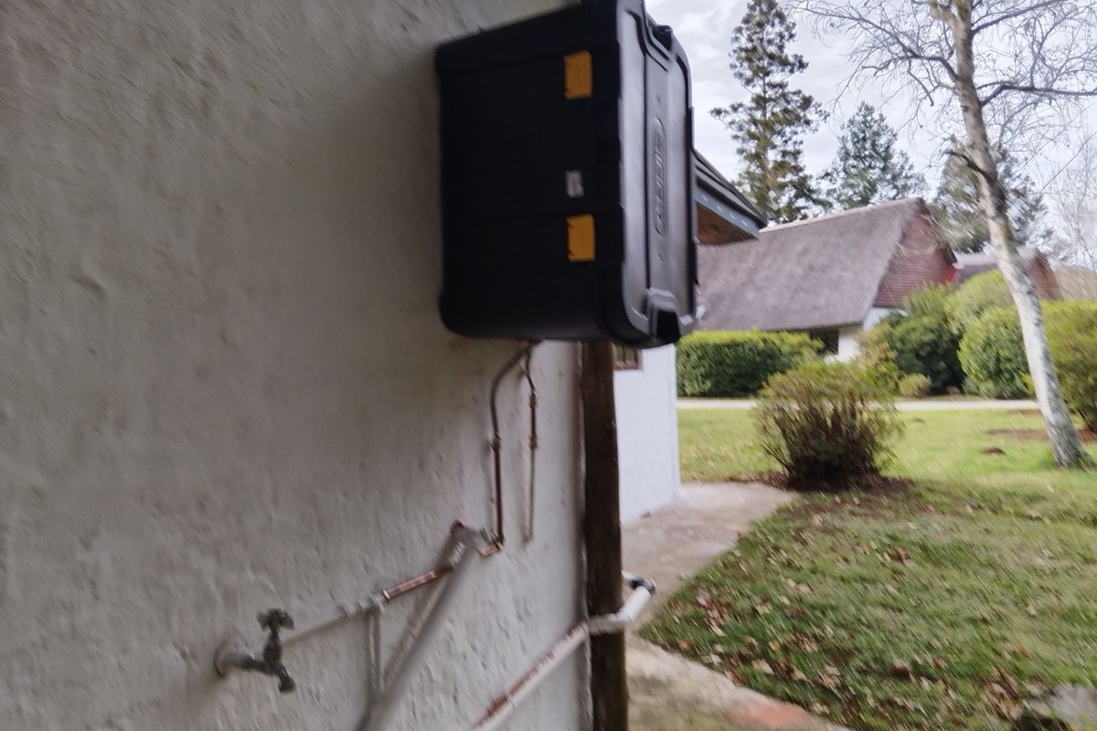 Exterior wall featuring an outdoor tap and exposed plumbing infrastructure, situated in a garden setting.