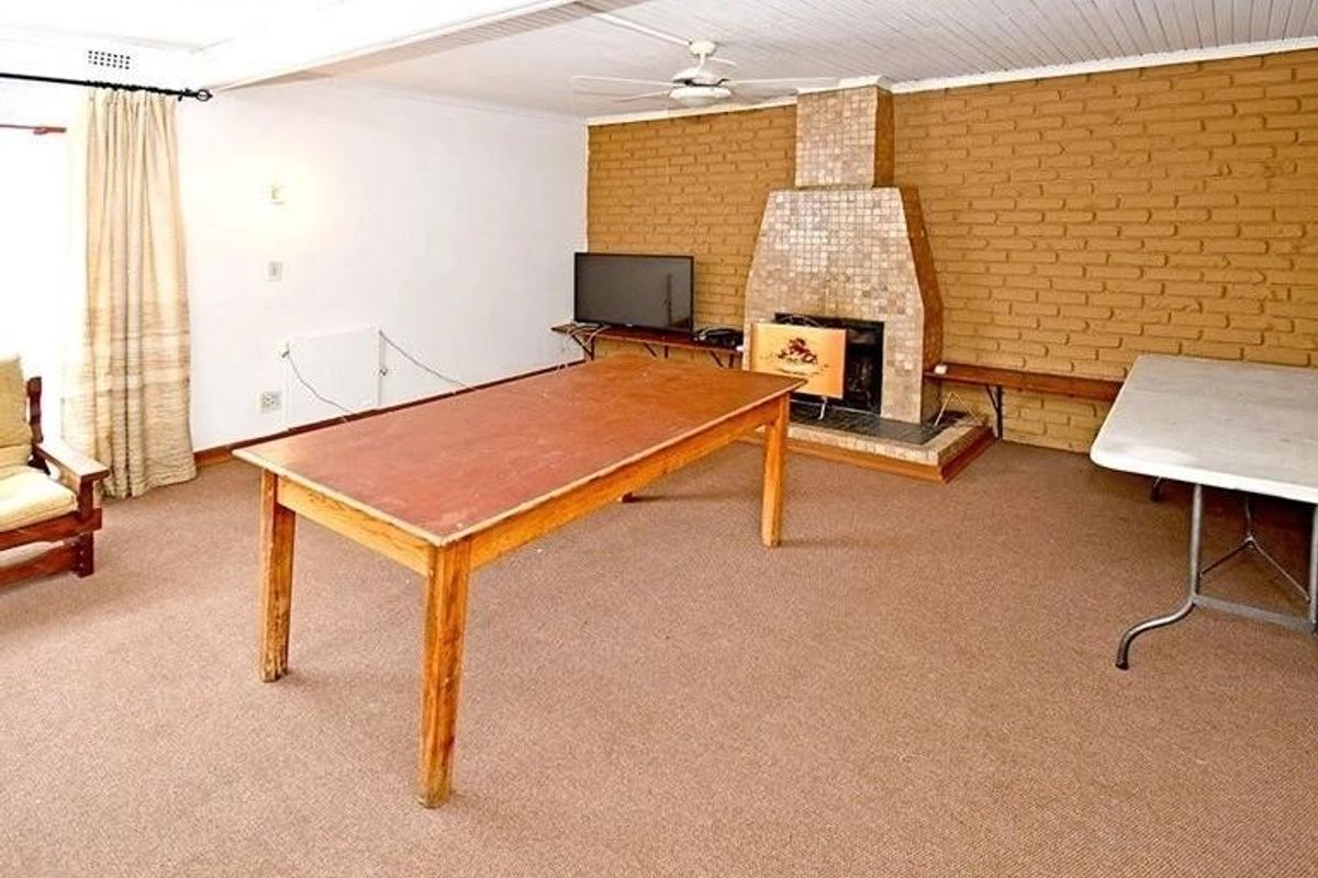 Spacious living room featuring a prominent brick fireplace with tiled hearth, carpeted flooring, and a white timber-paneled ceiling.