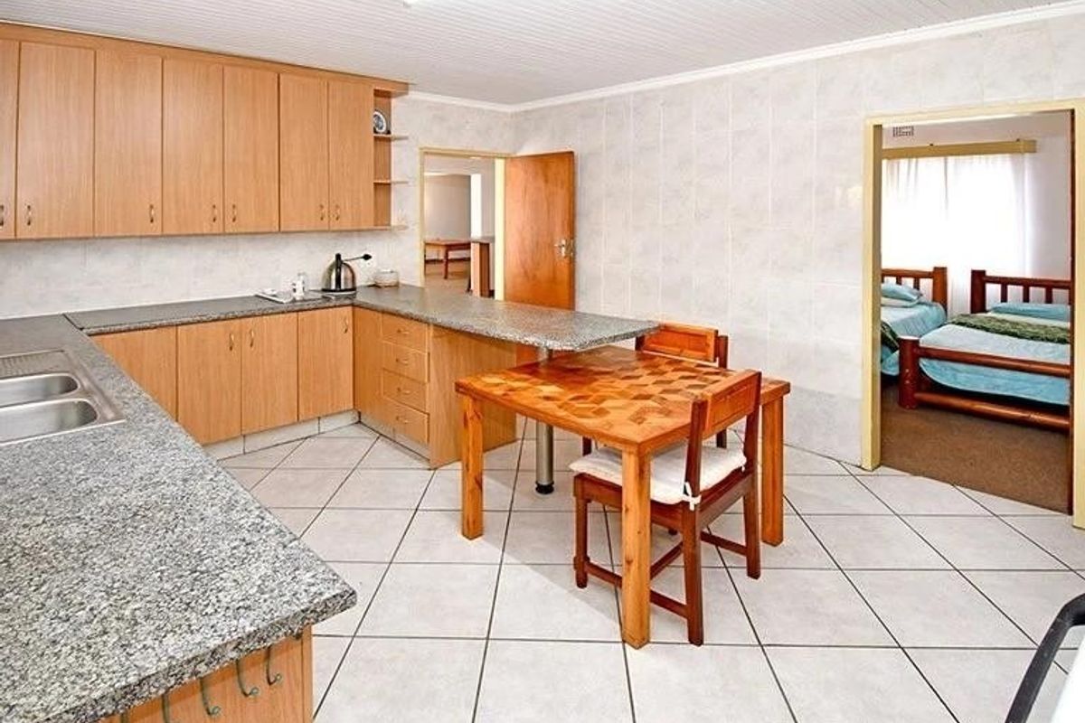 A functional kitchen featuring light wood cabinetry, granite-look countertops, and tiled flooring, with an integrated breakfast bar and direct access to adjacent rooms.