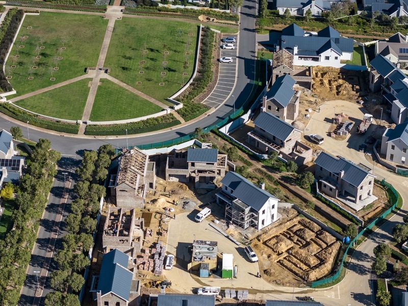 Aerial view of a residential estate under construction, showing multiple housing units in various stages of development alongside established infrastructure and parkland.