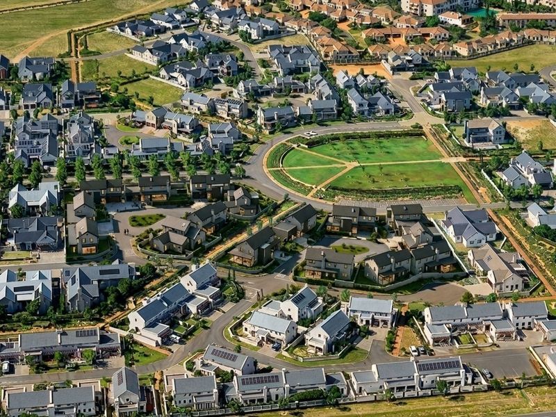 An aerial view of a well-planned residential estate featuring numerous detached homes, paved streets, and a central communal green space.