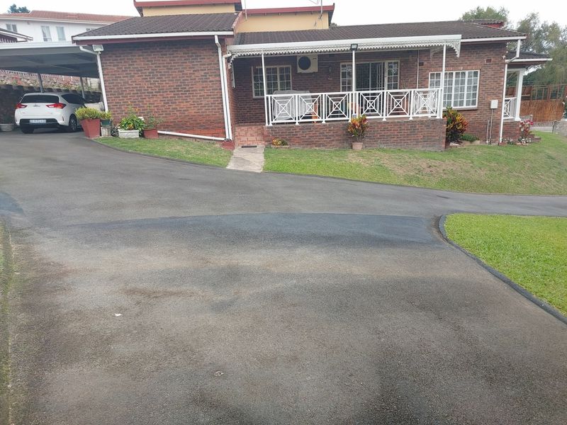 A brick-faced house featuring a covered patio, paved driveway, and carport, set within a landscaped residential garden.