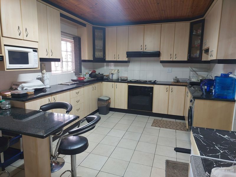 Functional kitchen featuring light wood cabinetry, dark granite countertops, built-in oven, hob, extractor fan, and tiled flooring.