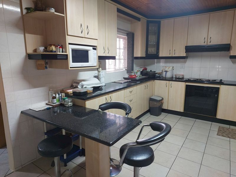 Functional kitchen featuring light wood cabinetry, dark granite countertops, integrated oven, hob, and extractor fan with a convenient breakfast nook.