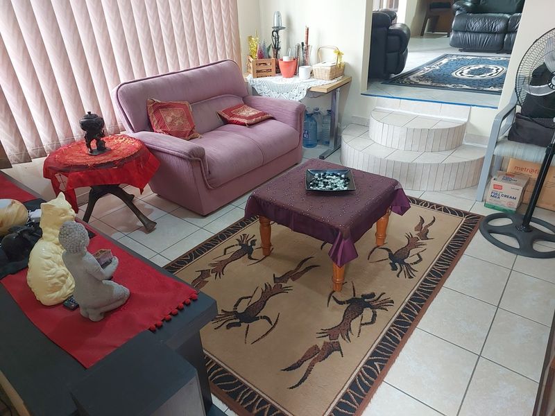 A living room area featuring tiled flooring and a raised step leading to an adjacent space, with vertical blinds covering the window.