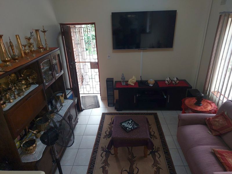 A living room featuring tiled flooring, a wall-mounted television, and a security gate leading to the exterior.