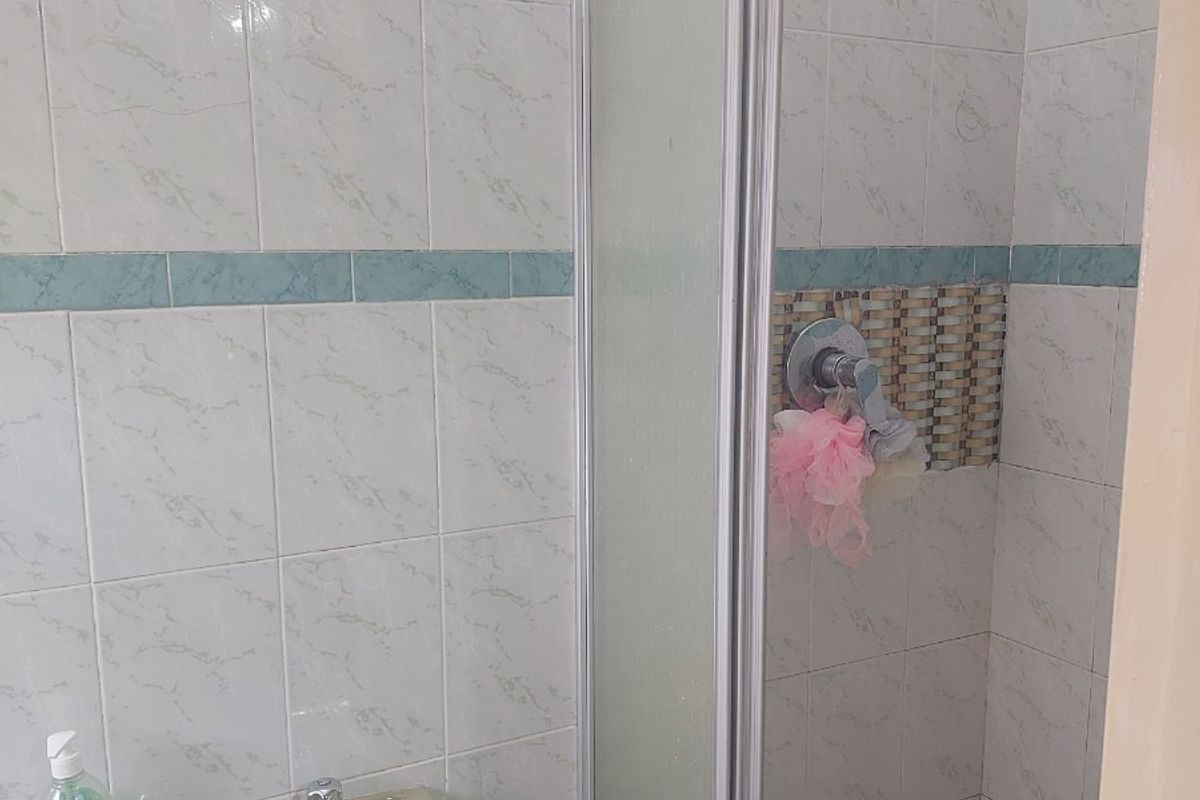 A functional bathroom featuring a pedestal basin, a glass-enclosed shower cubicle, and tiled wall finishes.