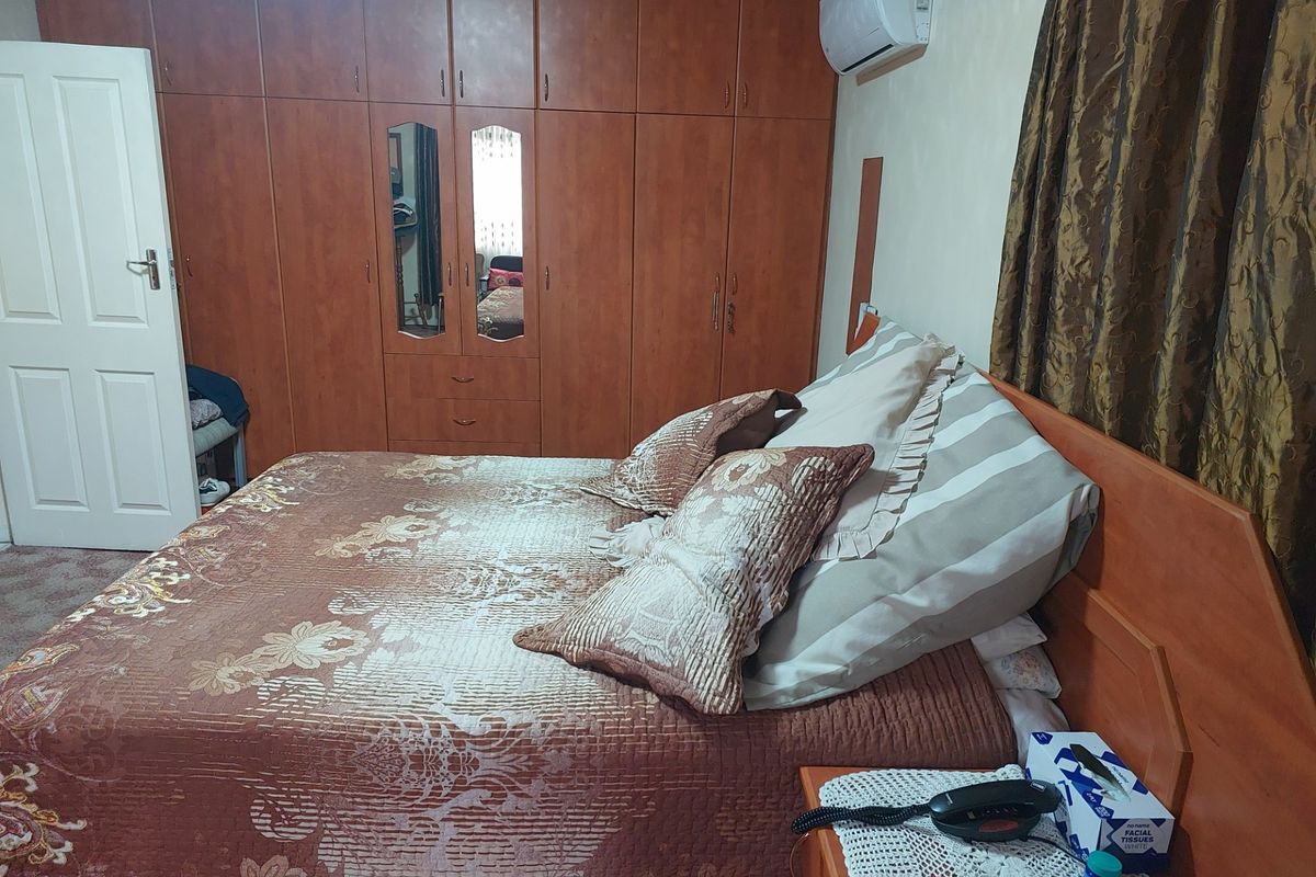 A bedroom featuring built-in wooden cabinetry with integrated mirrors and a wall-mounted air conditioning unit.