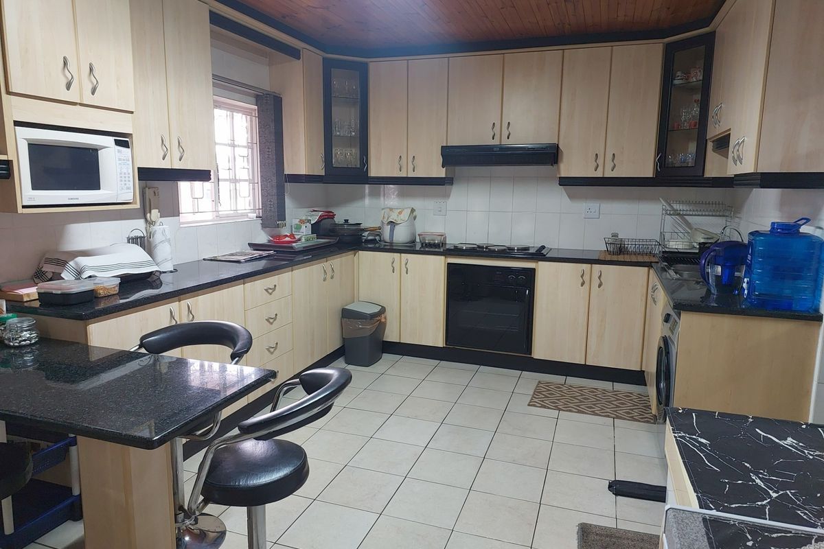 Functional kitchen featuring light wood cabinetry, dark granite countertops, built-in oven, hob, extractor fan, and tiled flooring.
