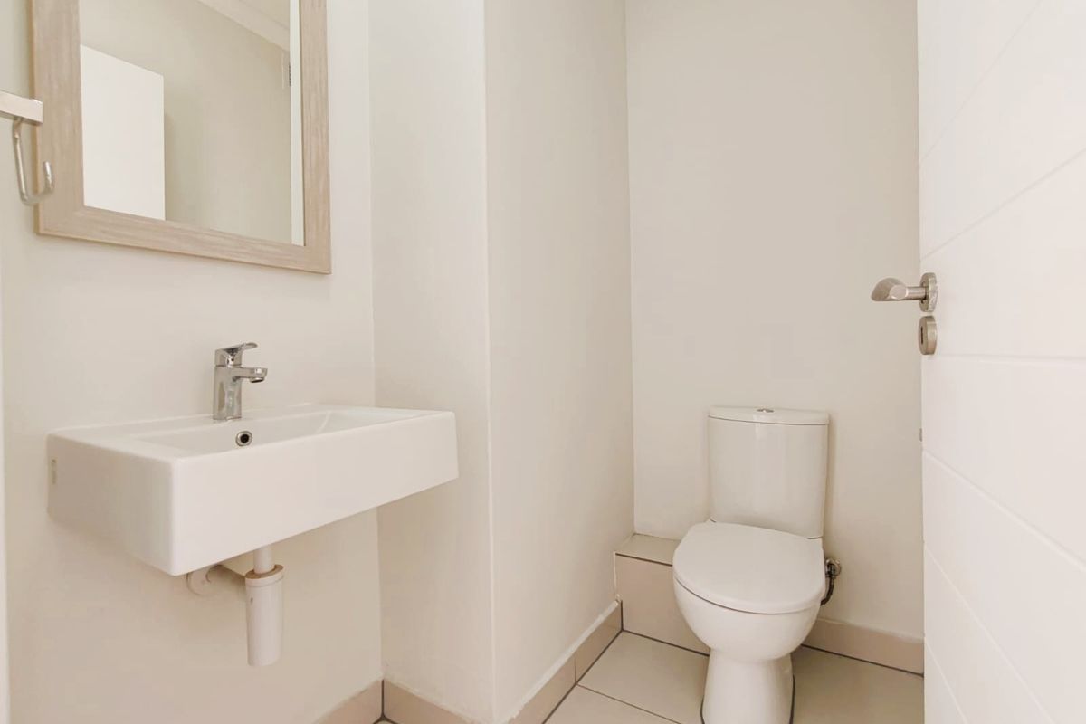 A clean and modern guest bathroom featuring a wall-mounted basin, a contemporary toilet, and a framed mirror.