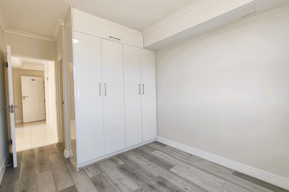 A bright bedroom featuring modern grey wood-look flooring and a large, floor-to-ceiling white built-in wardrobe with sleek handles.