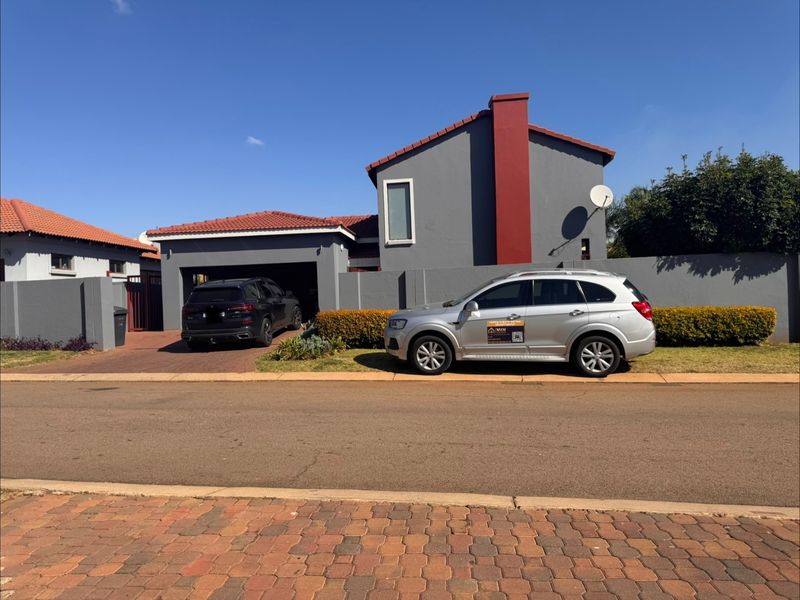 Front view of a residential house featuring a paved driveway, attached garage, and perimeter boundary wall.