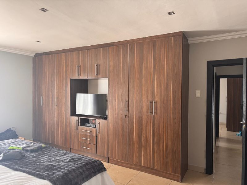 A bedroom featuring extensive floor-to-ceiling built-in wooden cupboards with an integrated media unit and recessed ceiling lighting.