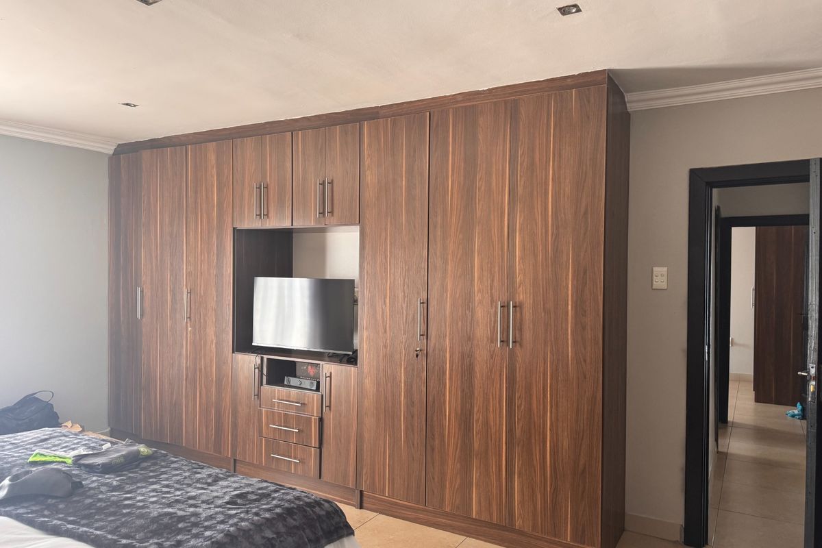 A bedroom featuring extensive floor-to-ceiling built-in wooden cupboards with an integrated media unit and recessed ceiling lighting.
