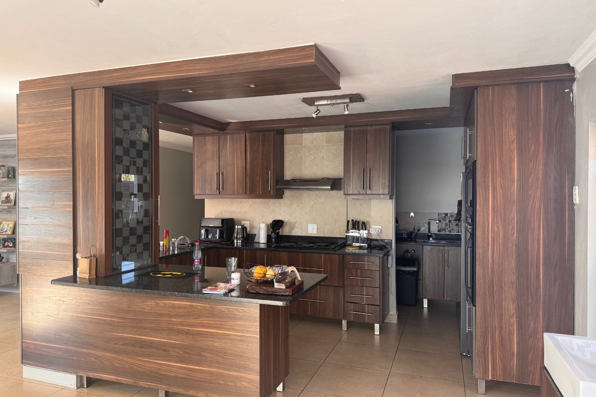 Modern kitchen featuring dark wood cabinetry, granite countertops, a breakfast bar, and an integrated scullery area with tiled flooring.