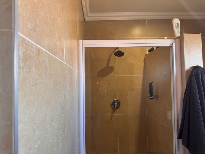 A functional shower enclosure featuring beige wall tiles, a chrome shower head, and a white-framed glass door.