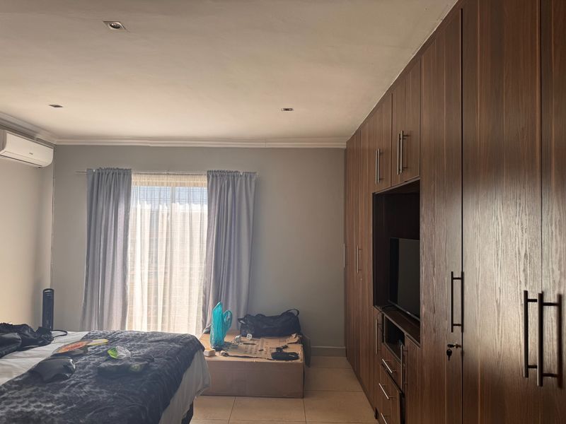 A well-lit bedroom featuring extensive built-in wooden cabinetry, tiled flooring, and a wall-mounted air conditioning unit.