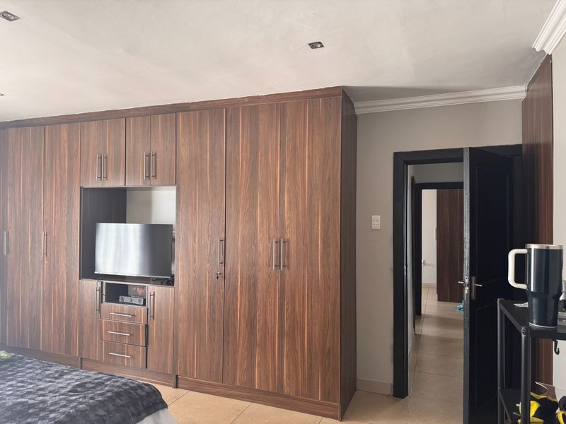 A bedroom featuring extensive dark wood built-in cupboards with integrated shelving and storage, complemented by tiled flooring and recessed ceiling lighting.