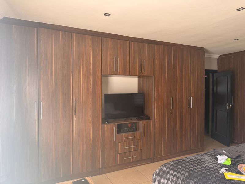 A bedroom featuring extensive floor-to-ceiling built-in wooden cabinetry with integrated shelving and storage, complemented by tiled flooring and recessed ceiling lighting.