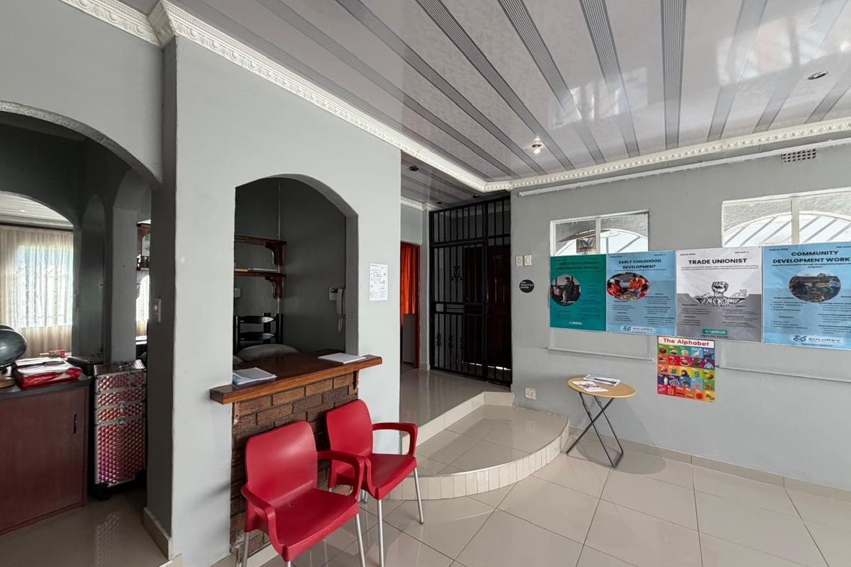 An interior view of a multi-purpose room featuring tiled flooring, a brick-faced service counter, and a raised platform area with security gate access.