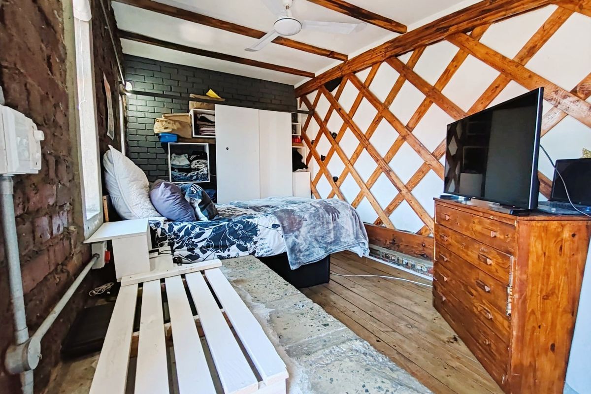 A rustic bedroom featuring exposed brick walls, timber ceiling beams, and a unique lattice wall design with wooden flooring.