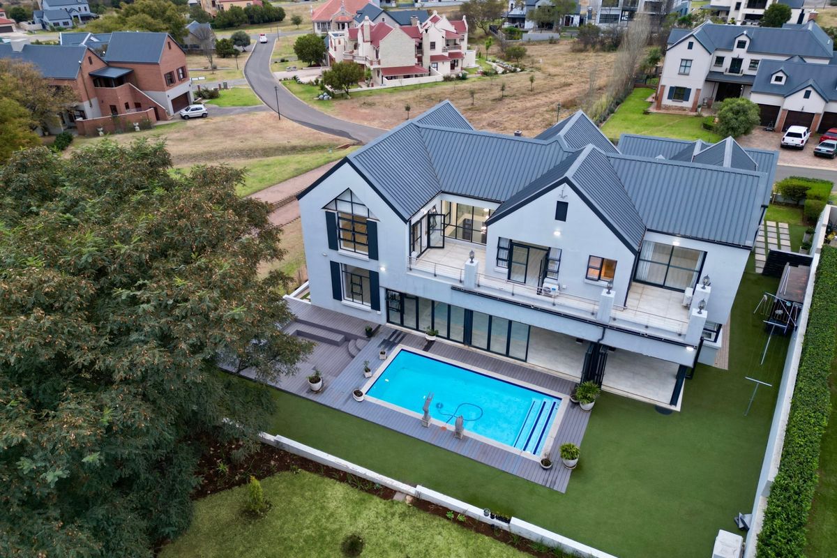 Aerial view of a modern double-story residence featuring a swimming pool, expansive timber decking, a large balcony, and a well-maintained garden.