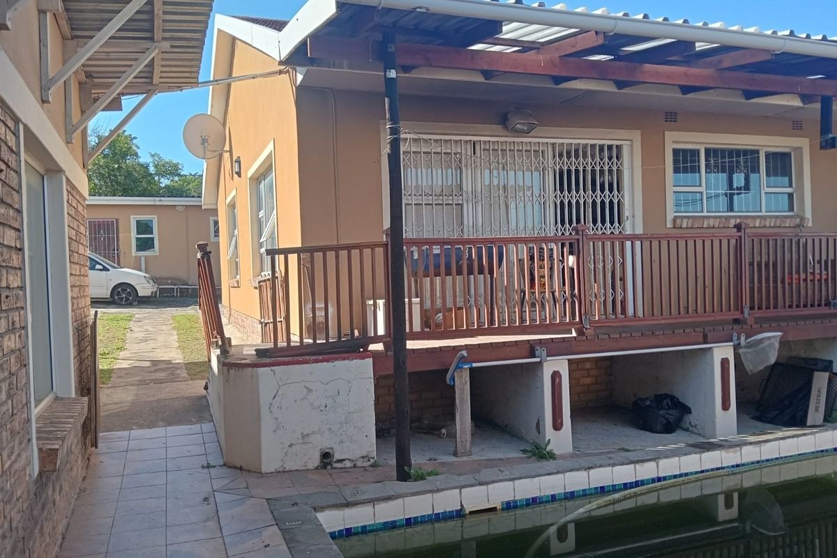 Rear exterior view featuring a raised timber deck, security gates, and an adjacent swimming pool area with paved surrounds.