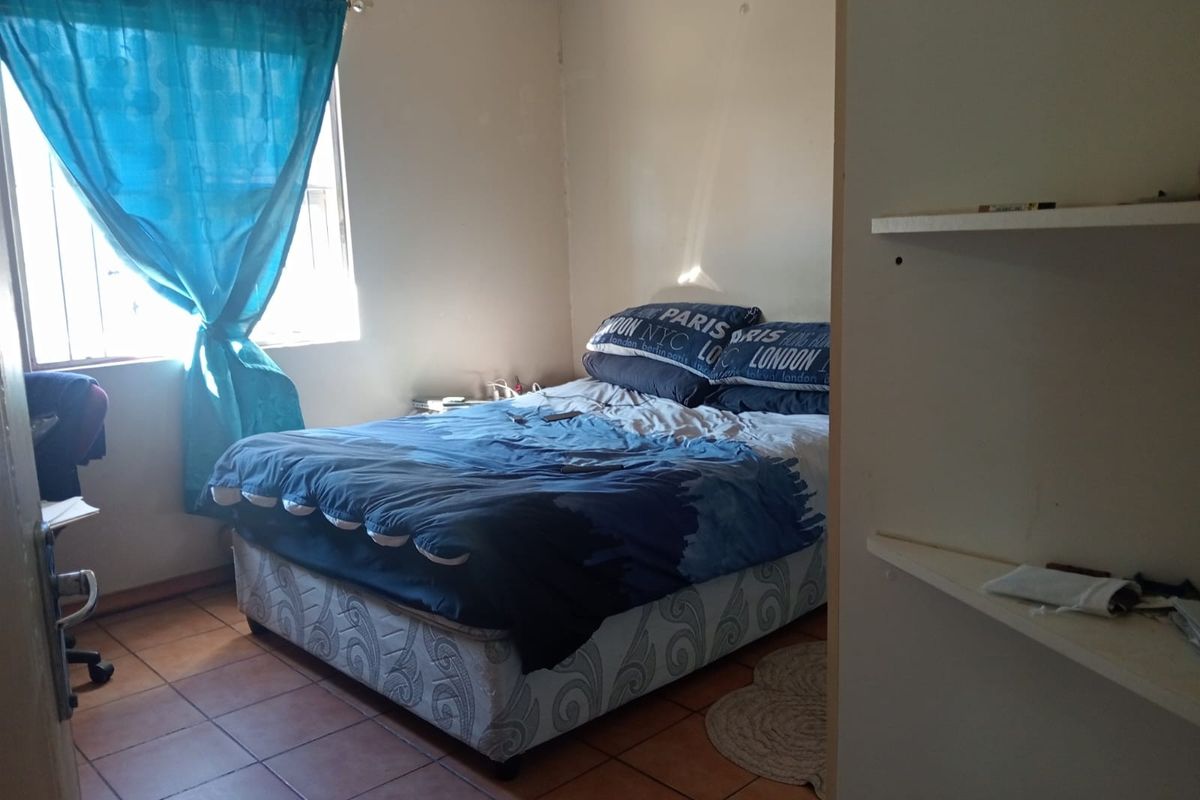 A bedroom featuring tiled flooring, a window with security bars, and built-in wall shelving.