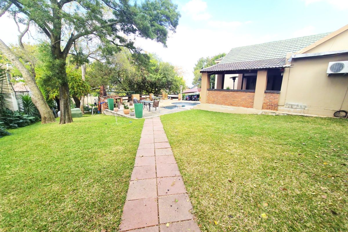 Spacious backyard featuring a manicured lawn, a paved pathway leading to a covered patio area, and an integrated swimming pool.