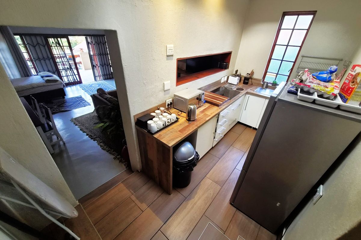 A compact kitchen featuring wooden countertops, white cabinetry, and tiled flooring, with an open-plan layout leading into an adjacent living and bedroom area.