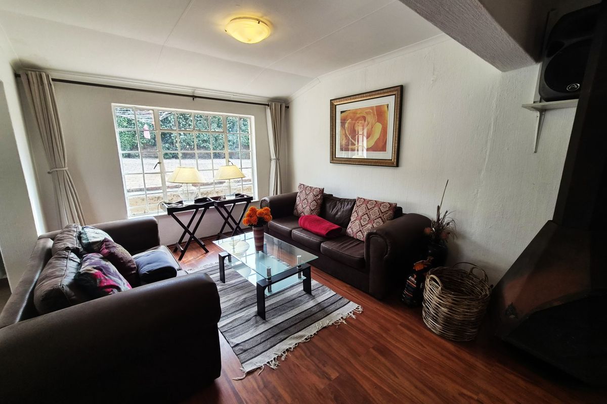 A cozy living room featuring warm wood-look flooring, a large window providing natural light, and a built-in fireplace.
