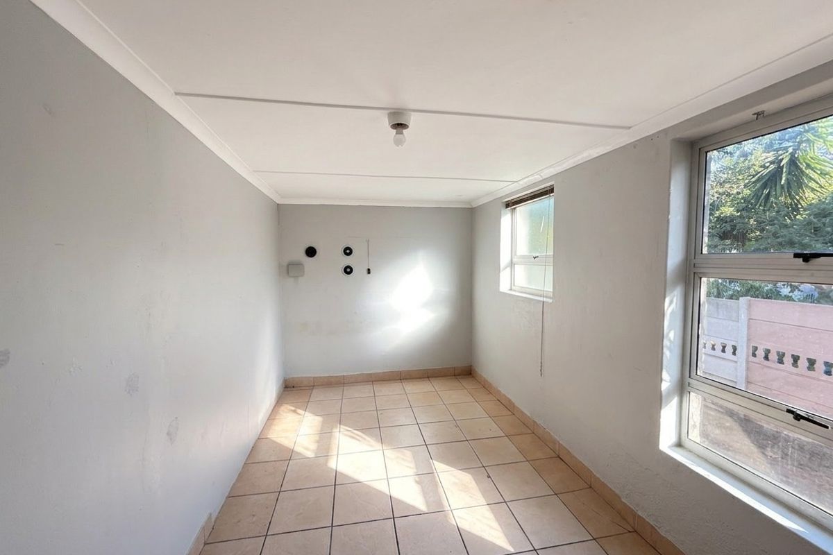 An empty, neutrally painted bedroom featuring tiled flooring and aluminium window frames, offering a blank canvas for potential renovation or staging.