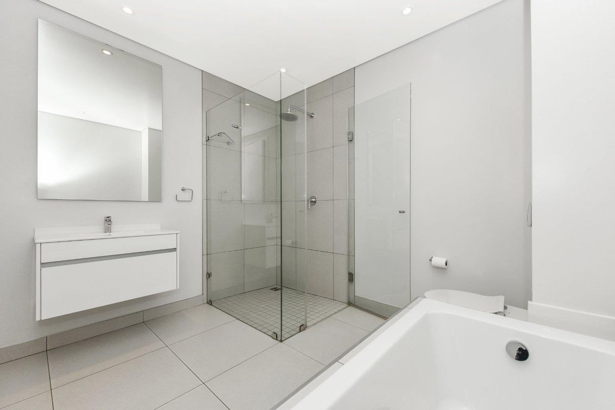 Modern bathroom featuring a glass-enclosed walk-in shower, a wall-mounted vanity with a basin, and a separate bathtub with neutral floor-to-ceiling tiling.