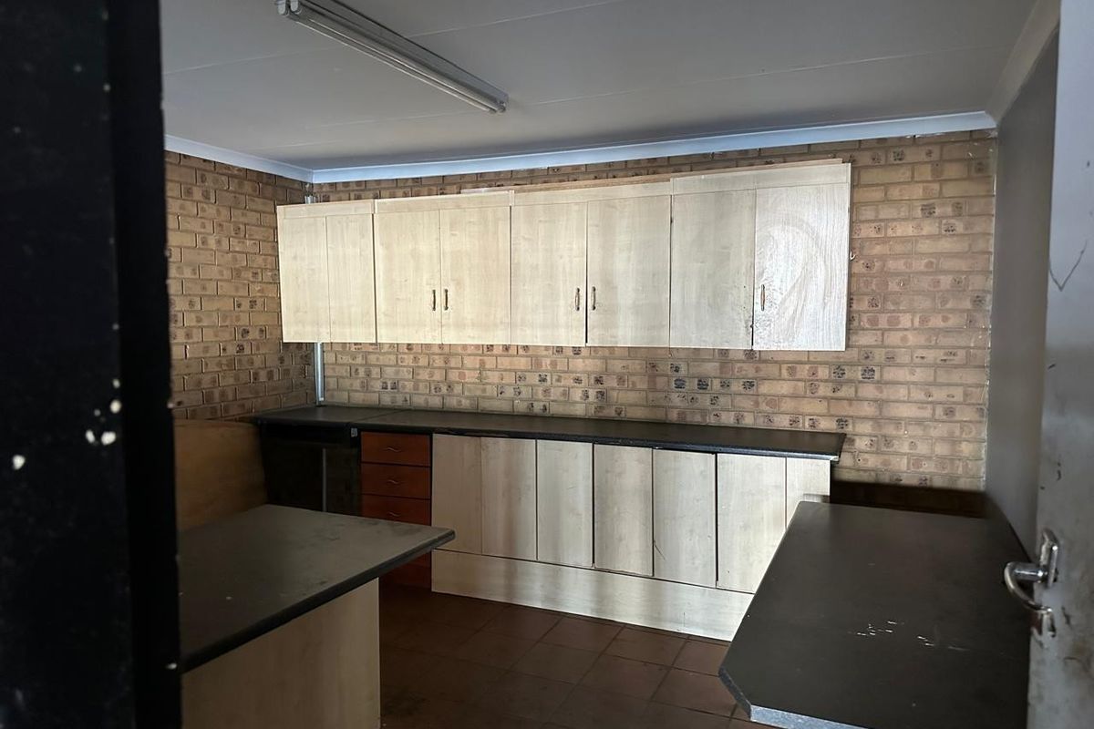 A functional utility or kitchen prep area featuring built-in cabinetry, laminate countertops, and exposed brick walls.